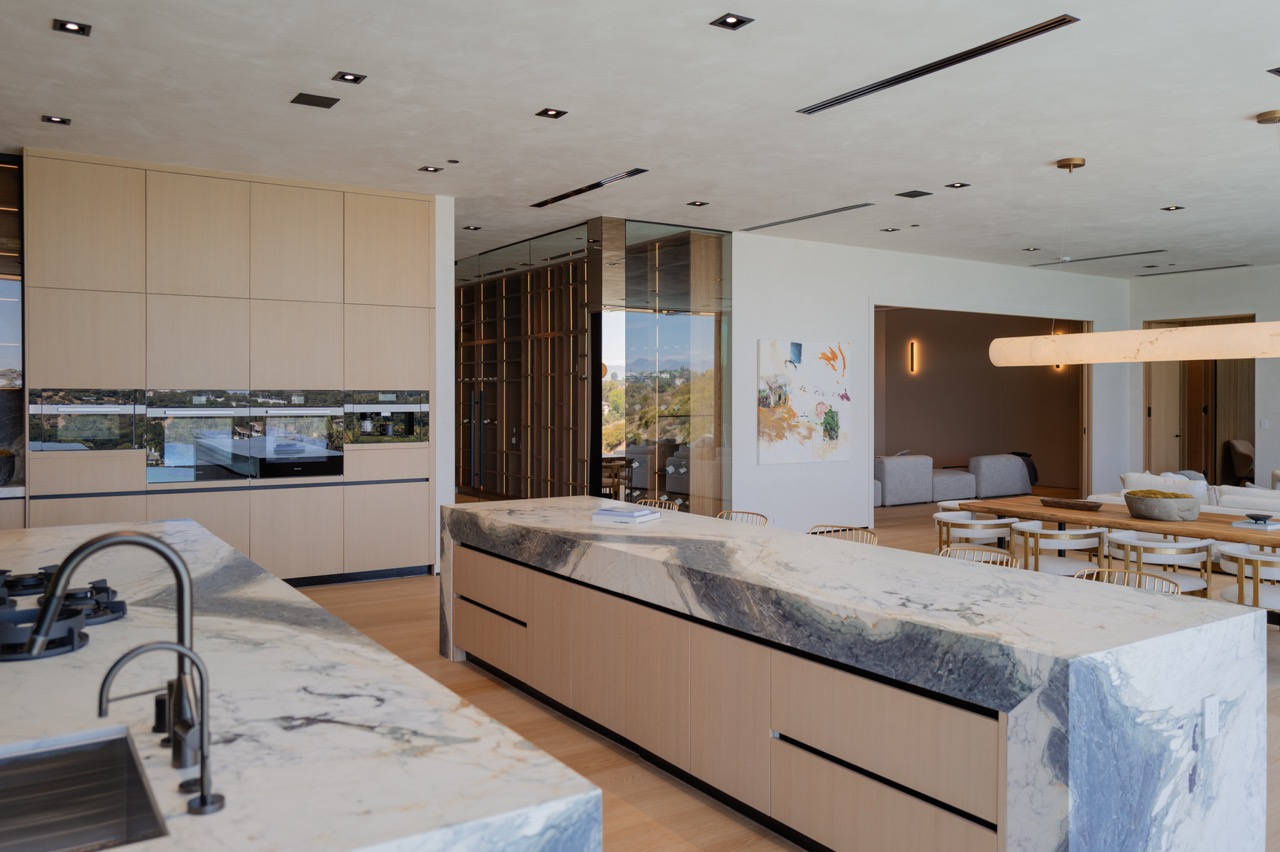 Pale oak kitchen with twin marble islands opening to a dining room and canyon view