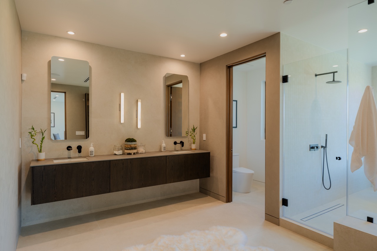 Primary bathroom with a wall-hung dark oak double vanity, limestone walls, and a walk-in glass shower